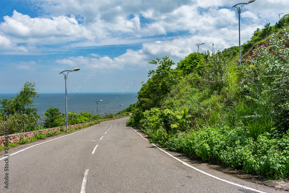 straight road going to downwards down of a mountain with blue ocean & blue sky background. 