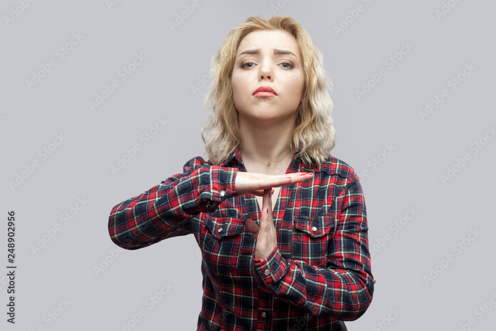 I need more time. Portrait of nervos beautiful blonde young woman in casual red checkered shirt standing with time out sign and looking at camera. indoor studio shot, isolated on grey background