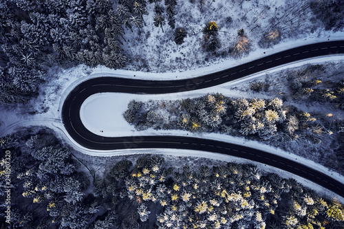 Aerial drone view of a curved winding road through the forest high up in the mountains in the winter with snow covered trees and curved streets in winter