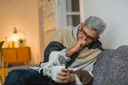 sick middle aged man coughing. sitting at his apartment photo