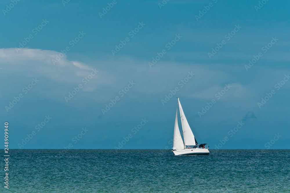 Front view, very long distance of a single sailboat underway on a windy, sunny, winter day on the gulf of mexico