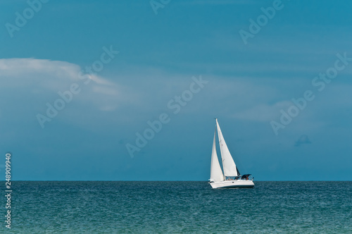 Front view, very long distance of a single sailboat underway on a windy, sunny, winter day on the gulf of mexico