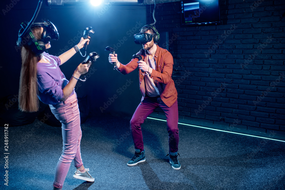 Fototapeta premium Mężczyzna i kobieta grają w gry przy użyciu zestawu słuchawkowego i gamepadów wirtualnej rzeczywistości w ciemnym pokoju klubu gry