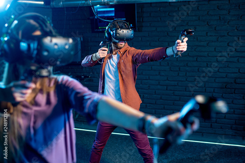 Man and woman playing game using virtual reality headset and gamepads in the dark room of the playing club photo