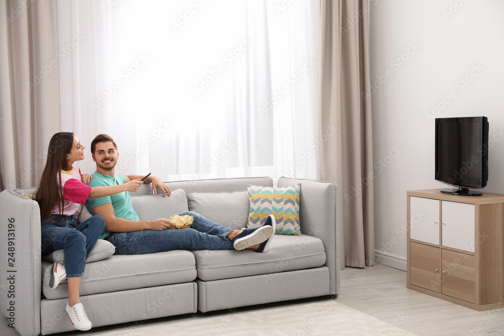 Couple with snack watching TV on sofa together at home. Space for text