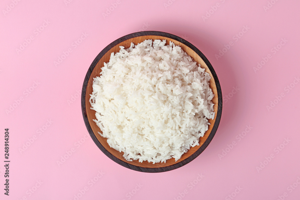 Bowl of boiled rice on color background, top view