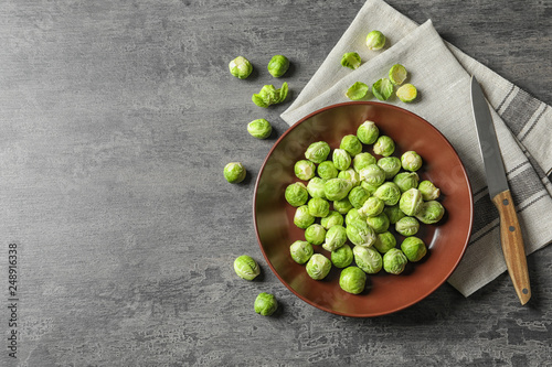 Plate of fresh Brussels sprouts, napkin and knife on grey background, top view with space for text