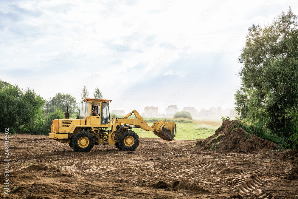 Fototapeta large yellow wheel loader aligns a piece of land for a new building. May be cut to banner or wallpaper with copy space.