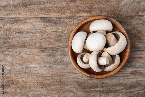Bowl of fresh champignon mushrooms on wooden background, top view with space for text