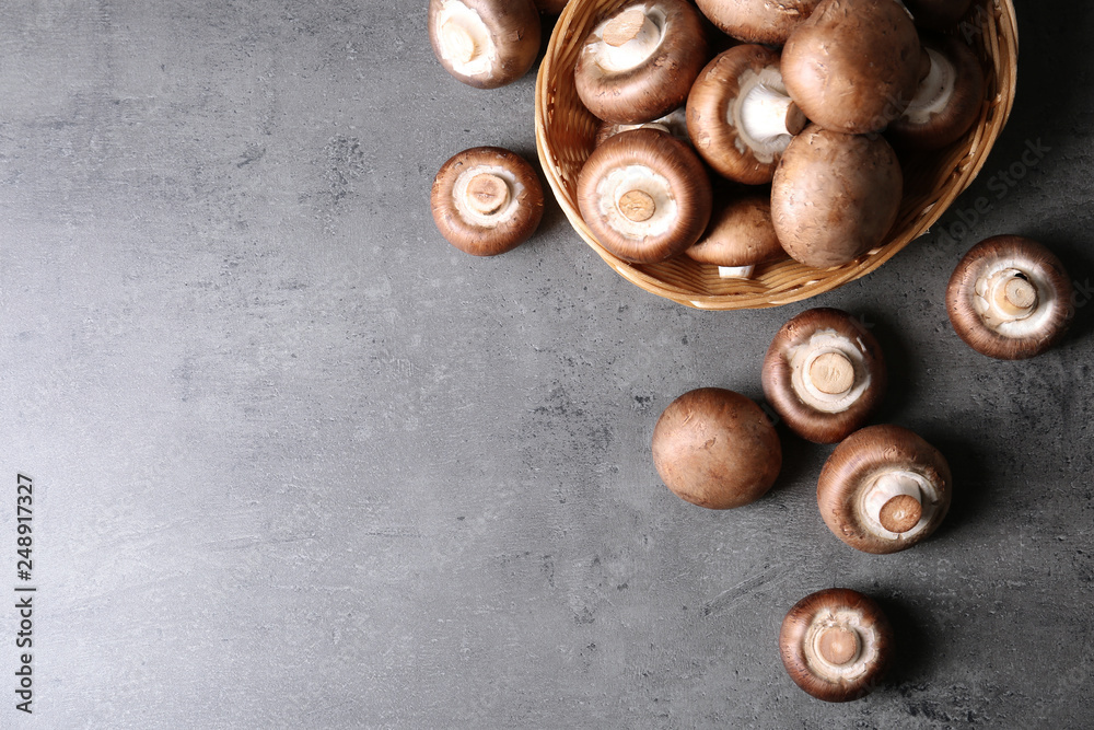 Obraz premium Wicker bowl and fresh champignon mushrooms on grey background, top view with space for text