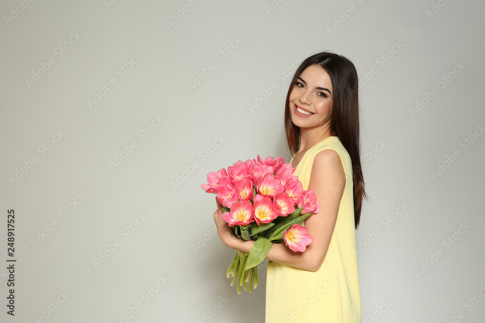 Portrait of beautiful smiling girl with spring tulips on light background, space for text. International Women's Day