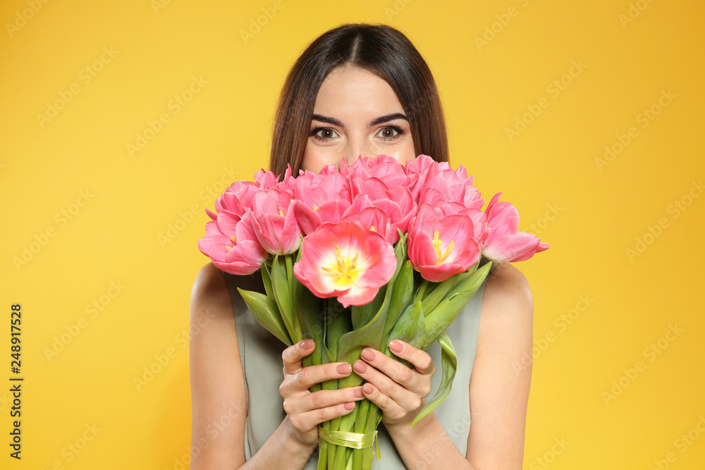 Beautiful girl with spring tulips on yellow background. International Women's Day