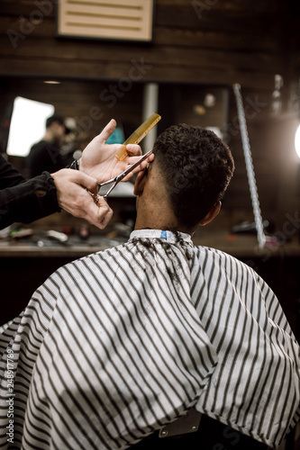 The barber scissors hair on the sides for a stylish black-haired man in the barbershop. Men's fashion and style