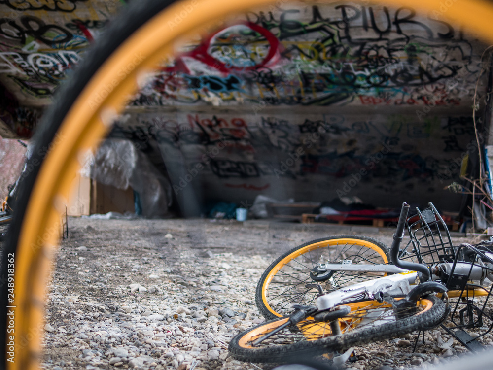 Old yellow scrap bicycles under concrete stairs with graffiti and homeless sleeping shelter