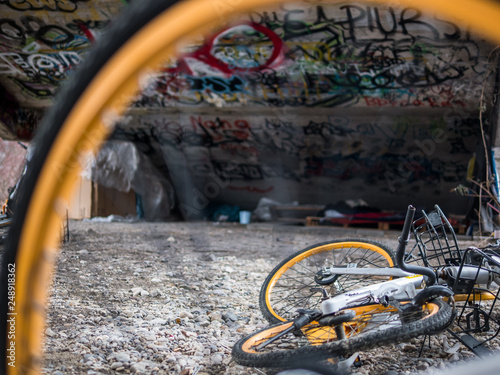 Old yellow scrap bicycles under concrete stairs with graffiti and homeless sleeping shelter