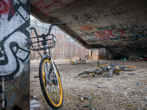 Old yellow scrap bicycles under concrete stairs with graffiti and homeless sleeping shelter