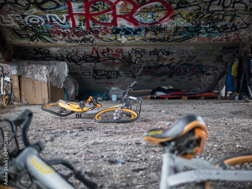 Old yellow scrap bicycles under concrete stairs with graffiti and homeless sleeping shelter