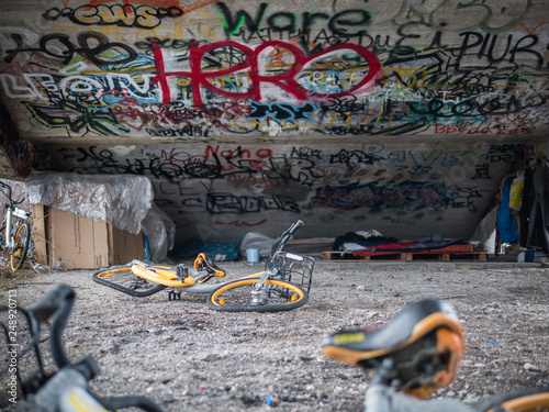 Old yellow scrap bicycles under concrete stairs with graffiti and homeless sleeping shelter