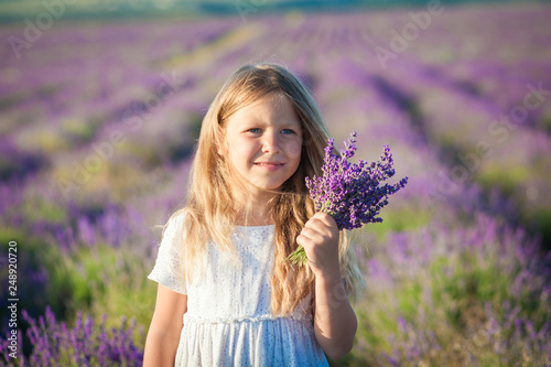 A girl in a white dress with a bouquet of lavender in her hands against the background of the field