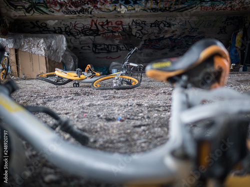 Old yellow scrap bicycles under concrete stairs with graffiti and homeless sleeping shelter