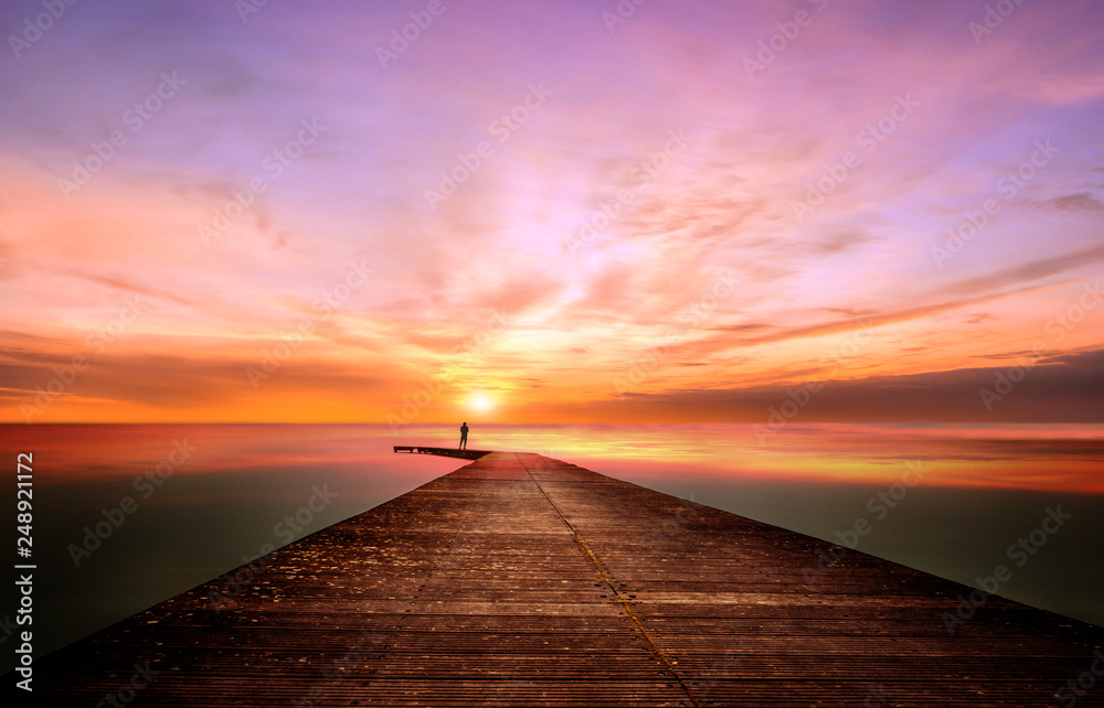 A person on a pier observes and contemplates a splendid sunset