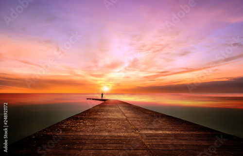 Fototapeta Naklejka Na Ścianę i Meble -  A person on a pier observes and contemplates a splendid sunset