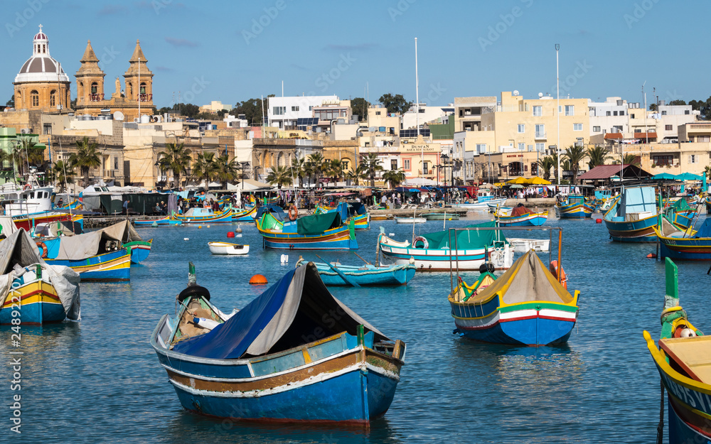 Marsaxlokk Harbour with Traditional, colorful Luzzu Boats in the bay with market in background. Marsaxlokk, Malta, Europe.