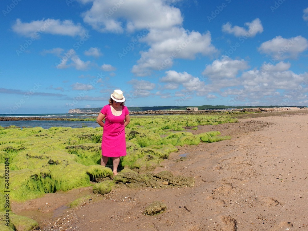 mujer con vestido rojo paseando por la playa con algas marinas verdes