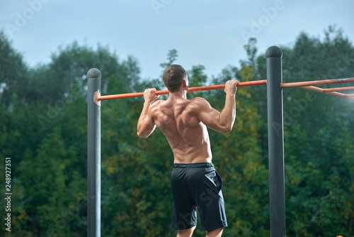 Strong shirtless man doing pull ups on horizontal bar.