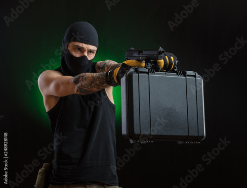 a man in a black mask with tattoos on his hands holding a gun and a case