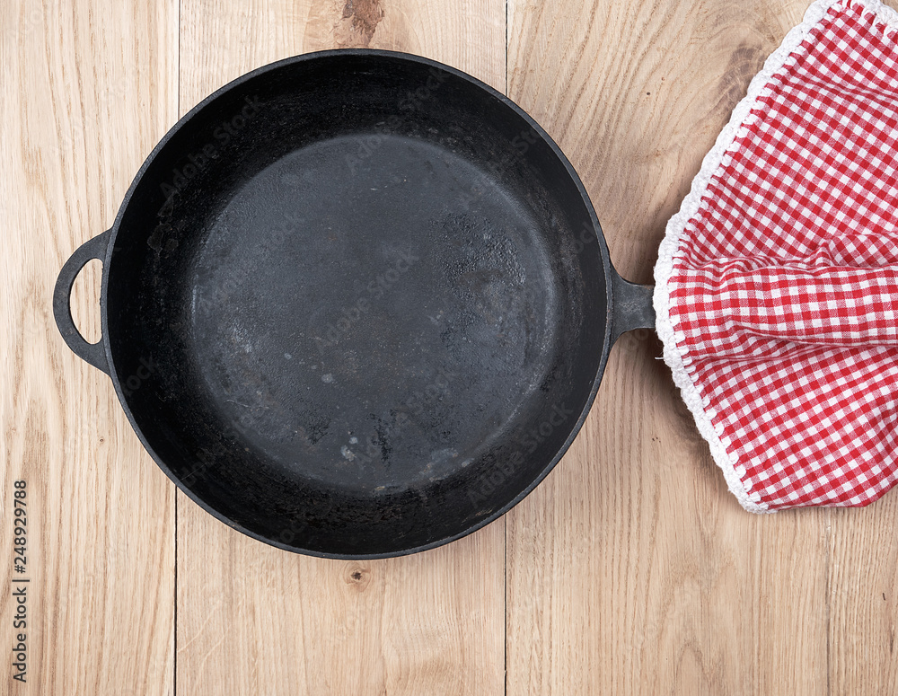 empty black round frying pan with wooden handle and red kitchen napkin empty black round frying pan with wooden handle and red kitchen napkin
