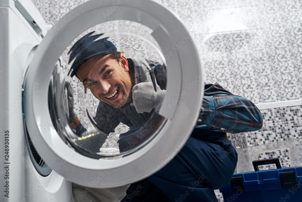 Glad of own results. Working man plumber in bathroom checking washing mashine Glad of own results. Working man plumber in bathroom checking washing mashine