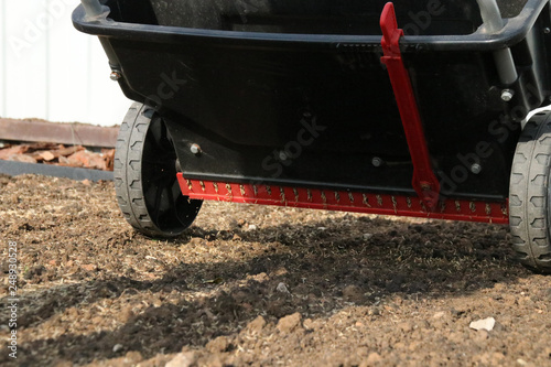 фотографія Sowing lawn grass seeds with a drop lawn spreader in the summer garden