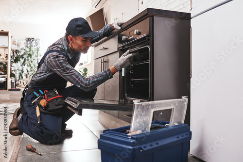 Don't delay with repair. Close-up of repairman examining oven photo