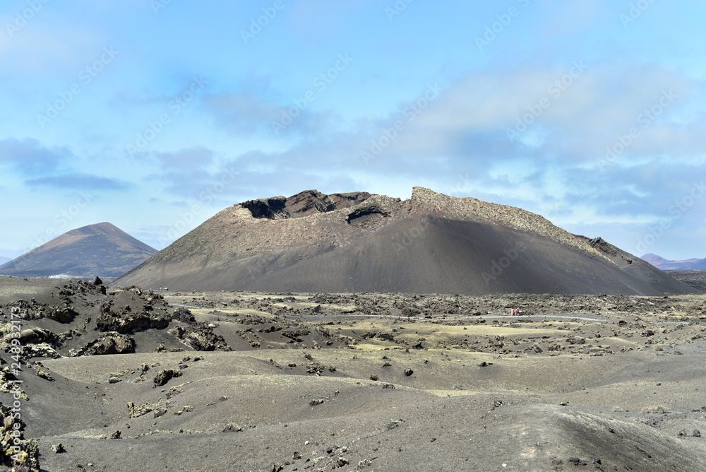 Scenic view of a Volcanic crater in the Timanfaya National Park under a blue sky with clouds. Lanzarote, Canary Islands, Spain