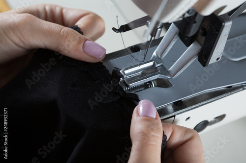 sewing process on sewing professional manufacturing machine with metal needle detailed by white caucasian woman's hands holding lace fabric for lingerie production