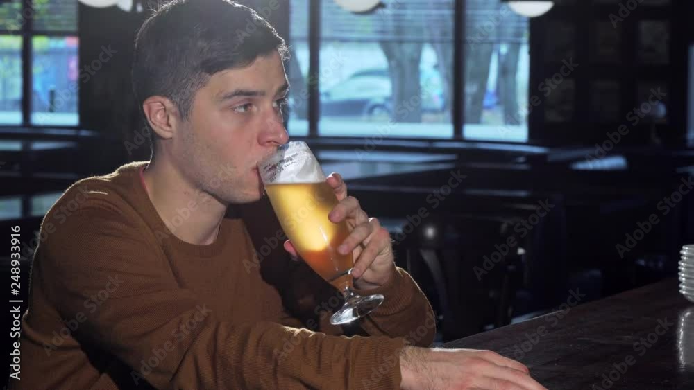 Young man smiling to the camera after sipping delicious beer from a glass. Man enjoying drinking tasty craft beer at the pub, relaxing in the evening. Lifestyle, leisure concept