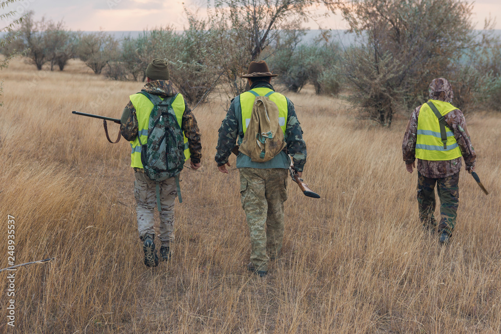 Hunter with a gun and a dog go on the first snow in the steppe, Hunting pheasant in a reflective vest Hunter with a gun and a dog go on the first snow in the steppe, Hunting pheasant in a reflective vest