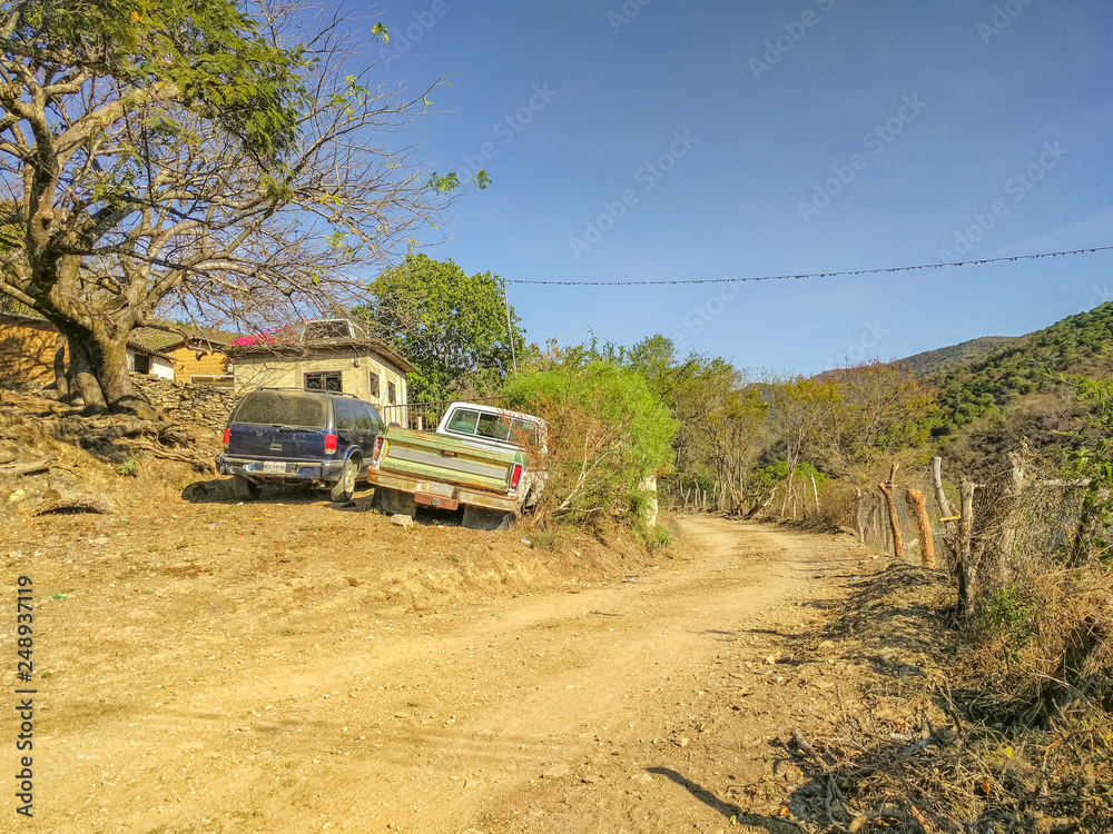 Two trucks are parked roadside along a dirt road unpaved road in Pipincatla of Ixcateopan. Rural streets in Guerrero. Travel in Mexico. Sierra Madre del Sur.
