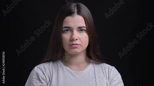 Portrait of young overweight brunette caucasian girl watching miserably into camera on black background. photo