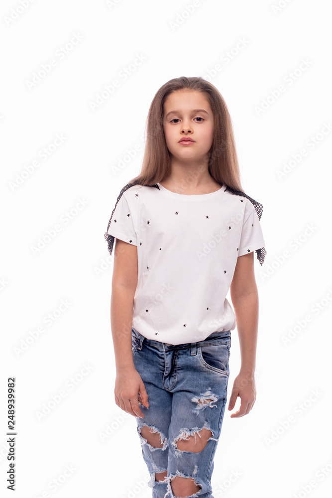 Obraz premium Studio shot of a little serious girl wearing jeans and white blouse on a white background. She is going