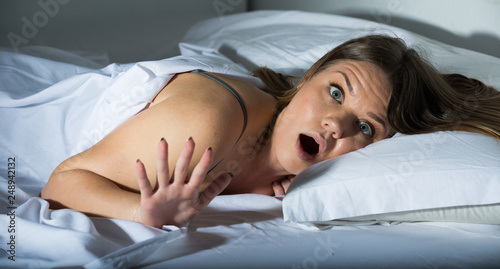 Young female is worried on bed, because oversleep in bedroom
