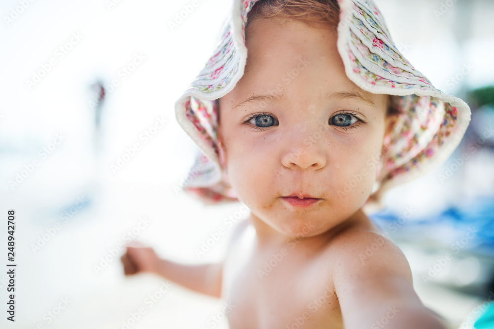 A close-up of small toddler girl sitting on beach on summer holiday. A close-up of small toddler girl sitting on beach on summer holiday.