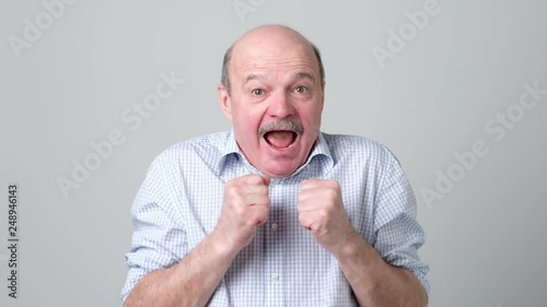 Senior man keeping clenched fists athis faces, shocked with good positive news. photo