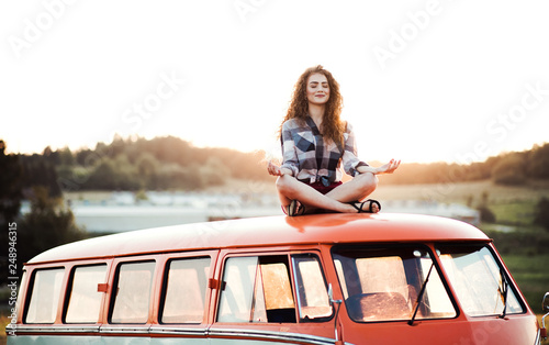 A young girl on a roadtrip through countryside, sitting on the roof of minivan doing yoga. photo