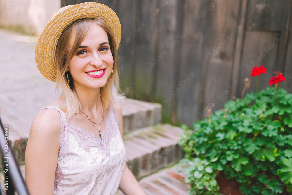 Attractive blonde girl with beautiful smile. A beautiful woman dressed in a straw hat and blue jeans sitting on the stairs.