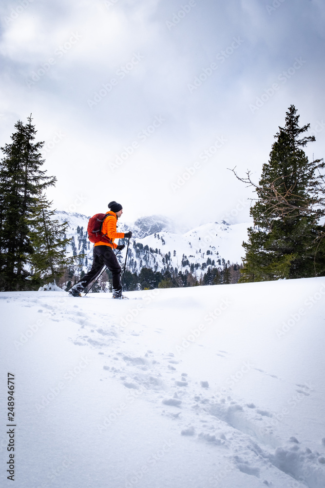 Man with orange jacket snowshoeing in Hohentauern on cloudy winterday