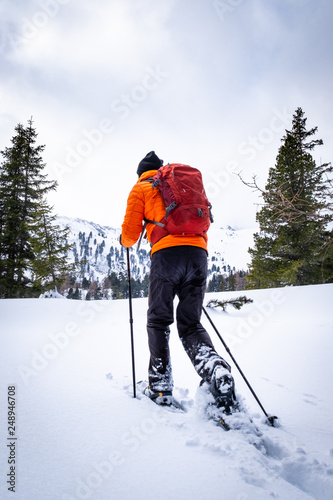 Man with orange jacket snowshoeing in Hohentauern on cloudy winterday photo