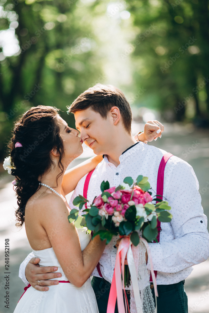 the bride and her husband are kissing in the park and holding beautiful wedding bouquet the bride and her husband are kissing in the park and holding beautiful wedding bouquet