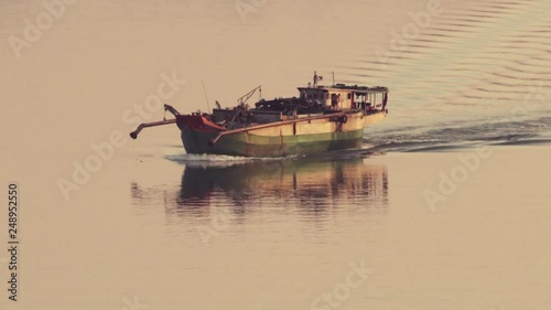 Sand dredger heading home at golden hour on the Mekong, camera follow photo